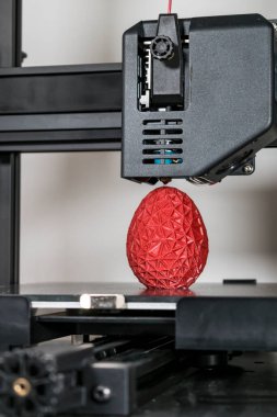 Close up of a 3d printer printing a red polygonal egg