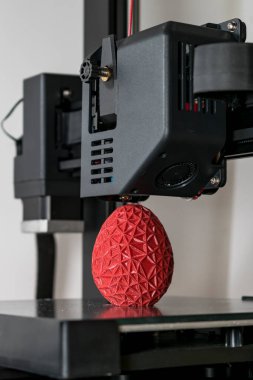 Close up of a 3d printer printing a red polygonal egg