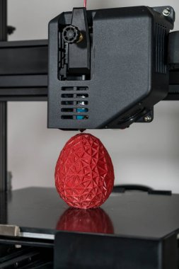 Close up of a 3d printer printing a red polygonal egg