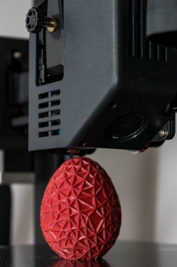 Close up of a 3d printer printing a red polygonal egg