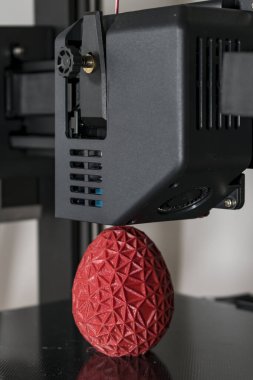 Close up of a 3d printer printing a red polygonal egg
