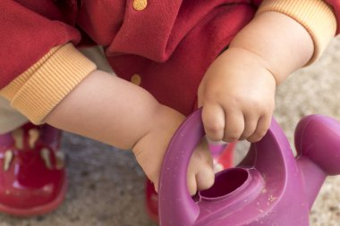 close up of a baby's hands playing with a watering can, outside activity, fine motor skills development