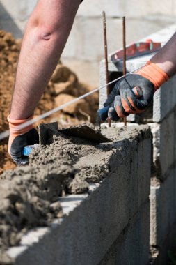 İnşaat alanına duvar örmek için beton döşeyen eldivenli bir duvarcı.