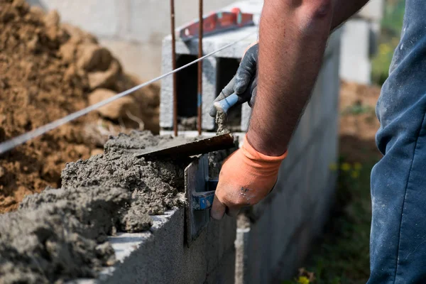 Bricklayer in glove spreading concrete to build a wall on construction site