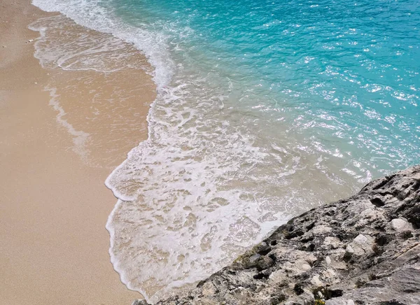 Солнечный мыс с бирюзовой волной, бьющей по белому бежевому песчаному побережью и серым известняковым скалам. Красочные морские воды с белой пеной на песчаном пляже. Камень, песок и море. — стоковое фото