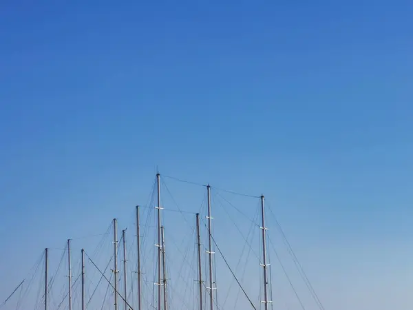 Многие высокие мачты многих яхт изолированы на ясном солнечном голубом фоне неба. Голубое небо с мачтами. Минималистские летние каникулы. — стоковое фото