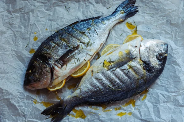 Fresh sea bream fish stuffed with lemon, salt and rosemary on crumpled bakig paper is ready for cooking.