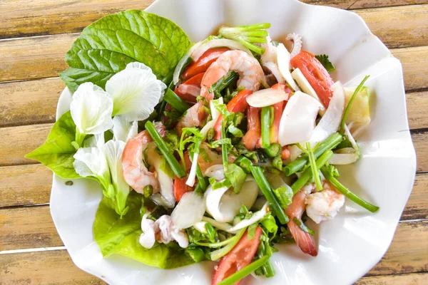 Tayland deniz ürünleri beyaz bir tabakta servis edilir ve bambu zemininde otlarla süslenmiş bir Tayland restoranında servis edilir.