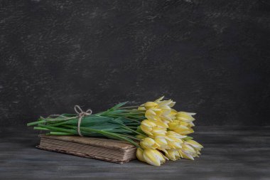 Durgun hayat. Lale buketi ve ahşap bir masanın üzerinde eski bir kitap. Kırsal biçim.