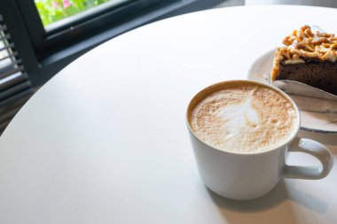 Beyaz masa arkasında sütlü ve sanat şekilli kahve fincanı, kopyalama alanı.