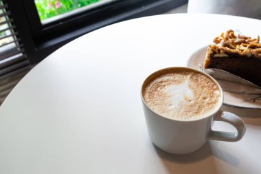 Beyaz masa arkasında sütlü ve sanat şekilli kahve fincanı, kopyalama alanı.