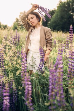 Beyaz keten gömlek ve şapka giymiş güzel bir kadın mavi ve beyaz çiçeklerle dolu bir tarlada yürüyor. Bahar. Yaz. Doğada 