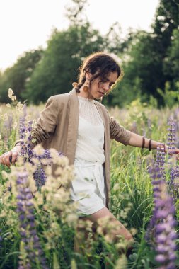 Beyaz keten gömlek ve şapka giymiş güzel bir kadın mavi ve beyaz çiçeklerle dolu bir tarlada yürüyor. Bahar. Yaz. Doğada 