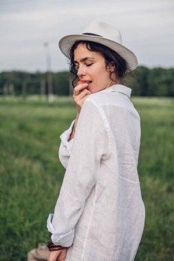 Beyaz keten gömlek ve şapka giymiş güzel bir kadın mavi ve beyaz çiçeklerle dolu bir tarlada yürüyor. Bahar. Yaz. Doğada 