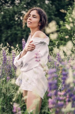 Beyaz keten gömlek ve şapka giymiş güzel bir kadın mavi ve beyaz çiçeklerle dolu bir tarlada yürüyor. Bahar. Yaz. Doğada 