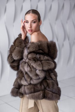 Güzel kadın tüylü bir kürke sarılı olarak beyaz stüdyoda fotoğraflandı. Ticari stil