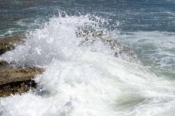 Splash wave rolls over ocean rocks