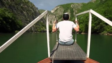 A young guy admires the canyon on a boat. Canyon Matka Skopje. Canyon in North Macedonia. Valley of the Treska River. Boat trip. Green rocky slopes. Transparent lake Matka with turquoise water.