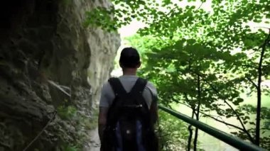 Genç bir adam Matka Kanyonu 'nda dağ yolunda yürüyor. Vadi boyunca dağ yolu. Matka Üsküp Kanyonu. Kuzey Makedonya 'daki kanyon. Yeşil kayalık yamaçlar. Bir adam dağlarda yürüyüş yapıyor..