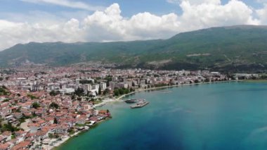 Drone view of the resort town of Ohrid. Drone shot overlooking Lake Ohrid and a small town against the backdrop of green mountains. A pier with boats in the center of Ohrid, a view from above.
