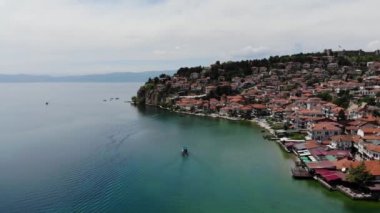 Drone view of the resort town of Ohrid. A shot from a drone with a view of a boat with tourists floating on Lake Ohrid against the background of a hilly shore. The old city from above.