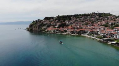 Drone view of the resort town of Ohrid. A shot from a drone with a view of a boat with tourists floating on Lake Ohrid against the background of a hilly shore. The old city from above.