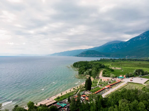 Ohri Gölü kıyısındaki kafe ve restoranların insansız hava aracı görüntüleri. Makedonya 'daki yeşil dağların insansız hava aracı manzarası. Makedonya 'nın kuzeyindeki Ohri Gölü' nün kumlu plajı.