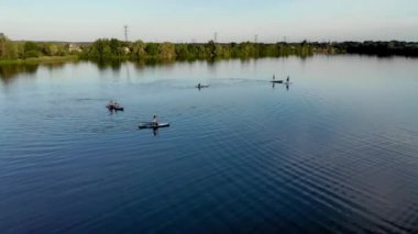 Drone view of people floating on a sub board on a blue lake. People have fun floating on a board on a lake on a hot day. Rest on the river. Enjoy your time. Drone shot on a large lake
