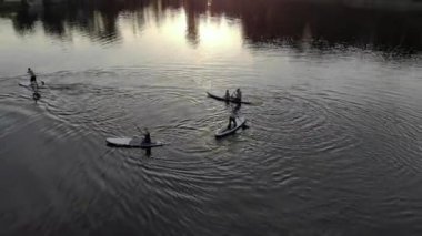 Mavi bir gölün üzerinde yüzen insanların insansız hava aracı görüntüsü. İnsanlar sıcak bir günde gölde sörf tahtasında yüzerken eğlenirler. Nehirde dinlen. Keyfinize bakın. İnsansız hava aracı büyük bir göle ateş etti.