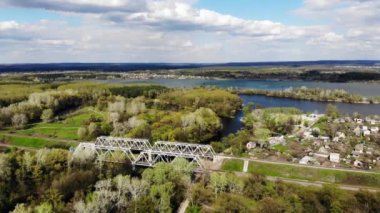 Panoramic view from a drone of the railway bridge over the river in a picturesque location. Blue lakes from above. Forest near the lake. A village next to a railway and a lake in northern Europe.
