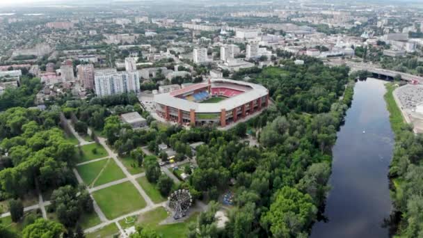 Panorámás kilátás egy futballstadion drónjáról Sumy városában. Egy stadion Észak-Európában. Egy drón lövése egy folyón és egy város Ukrajnában. Zöld park óriáskerékkel.