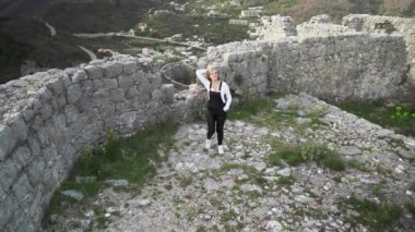 Harap olmuş Hac Nehai Kalesi 'nde bir kız yürüyor. Sutomore Karadağ' daki kale. Kız, dağların arka planında poz veriyor. Dağlarda yürüyüş. Ortaçağ Kalesi. 