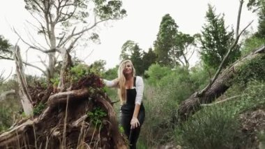 Genç bir kız Karadağ dağlarında yürüyor. Dağlarda düşen bir ağacın yanında poz veren güzel bir sarışın. Büyük bir ağacın kökü. Dağ yoluna çıkacağız. Dağlarda yürüyüş..