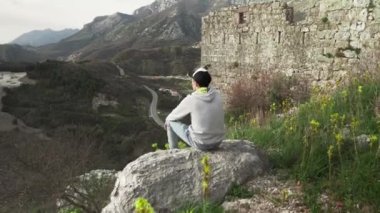 Genç bir adam, bir vadi ve dağların arkasındaki harabe Haj Nehai kalesindeki dağ manzarasına hayran. Adam Karadağ dağlarının arka planında poz veriyor. 