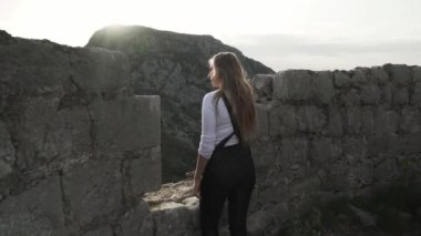 Harap olmuş Hac Nehai Kalesi 'nde bir kız yürüyor. Sutomore Karadağ' daki kale. Kız, dağların arka planında poz veriyor. Dağlarda yürüyüş. Ortaçağ Kalesi. 