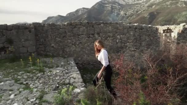 少女はサトモア モンテネグロのHaj Nehai Fortressの老朽化した要塞を歩き回っています 少女は山を背景にポーズをとる 山の中でハイキング 中世の要塞 — ストック動画