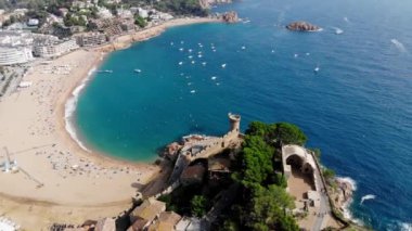 Tossa de Mar 'daki deniz manzaralı kalenin drone görüntüsü. İspanya 'da bir belediyenin insansız hava aracı çekimi. İnsanlar İspanya 'da kumlu bir plajda dinleniyor. Akdeniz yakınlarındaki bir kaplıca kasabası