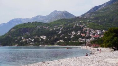 Bar Montenegro 'da dağ manzaralı çakıl taşı plajı. Baraj seti. İnsanlar deniz kenarında plajda dinleniyorlar. Karadağ 'daki yeşil dağlar ve deniz manzarası. Sakin ve rahat sahil kasabası. 