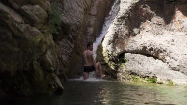 Adam Karadağ 'ın Eski Barı' ndaki şelalenin altında duruyor. Su dağlardan küçük bir gölete akar. Temiz ve şeffaf dağ suyu. Dağlarda küçük bir gölet 