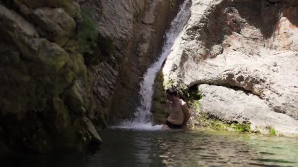那家伙站在黑山老酒吧的瀑布下 水从山上流到一个小池塘里 清澈透明的山水 山中的一个小池塘 — 图库视频影像