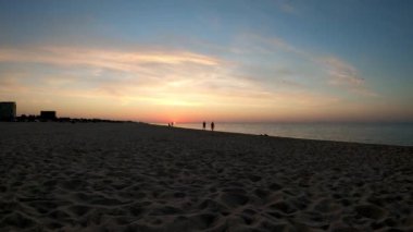 Odessa 'daki Karadeniz' de gündoğumunun gecikmesi. Hızlandırılmış gündoğumu ve günbatımı videoları. İnsanlar deniz kıyısında kumlu sahil boyunca yürür.