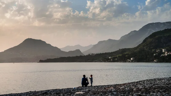 Dad takes a picture of his son on the phone on the beach near the sea against the backdrop of mountains.Sunset with mountain views in Bar Montenegro. Embankment of Bar. Resort town