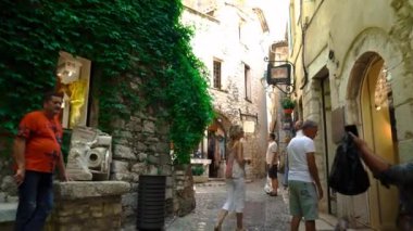 Saint-Paul-de-Vence 'in ortaçağ güçlendirilmiş köyü. İnsanlar Saint-Paul-de-Vence 'de dar bir sokakta yürüyor. Dar bir sokakta hediyelik eşya dükkanları ve galeriler 