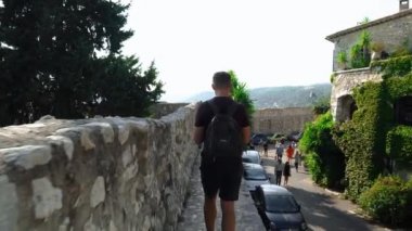 Güney Fransa 'da bir ortaçağ şehrinin duvarları boyunca yürüyen bir adam. Saint-Paul-de-Vence 'in ortaçağ köyü. Saint-Paul-de-Vence 'de insanlar sokakta yürüyor