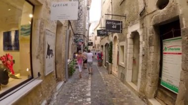 Saint-Paul-de-Vence 'in ortaçağ güçlendirilmiş köyü. İnsanlar Saint-Paul-de-Vence 'de dar bir sokakta yürüyor. Dar bir sokakta hediyelik eşya dükkanları ve galeriler 