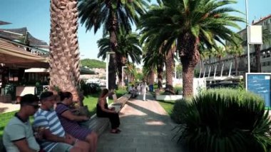 Embankment Riva in Split Croatia. People are resting on a bench near palm trees. Cafes and restaurants along the boulevard in Split Croatia. Popular place for walking