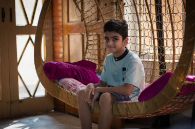 An Asian boy sitting in cradle at home