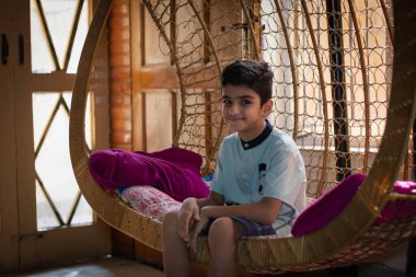 An Asian boy sitting in cradle at home