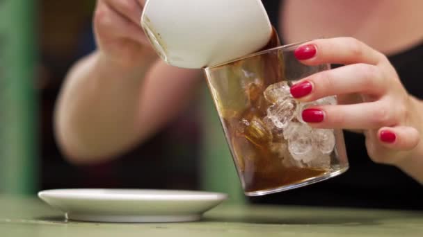 Κορίτσι ρίχνει καφέ από μια κούπα σε ένα ποτήρι με πάγο — Αρχείο Βίντεο
