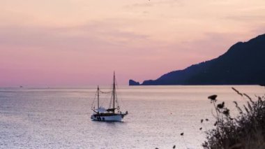 Vahşi doğada gün batımında küçük dalgalarda sallanan eski bir yat.